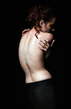 Dramatic portrait of a sad young woman among the dark. Rear view