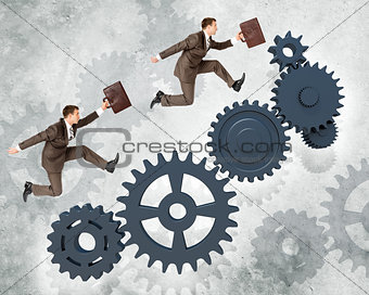 Two businessmen running on wheel gears