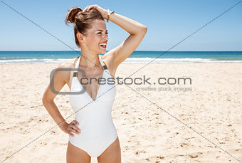 Happy woman in white swimsuit at sandy beach looking aside