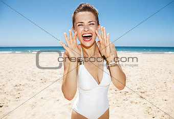 Woman shouting through megaphone shaped hands at sandy beach