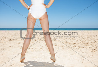 Closeup on legs of woman in white swimsuit at sandy beach