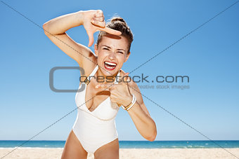 Happy woman in white swimsuit at sandy beach framing with hands