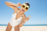 Woman in pineapple glasses showing victory gesture at beach
