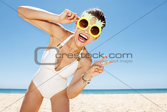 Woman in pineapple glasses showing victory gesture at beach