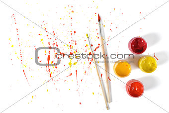 Gouache jars and paint brushes on a white background with colorful spray in top view
