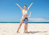 Happy mother and child in swimsuits at sandy beach rejoicing