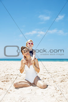 Happy mother and girl in swimsuits at sandy beach on a sunny day