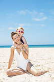 happy mother and child in swimsuits at sandy beach on sunny day