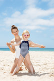 Smiling mother and child in swimsuits playing at sandy beach