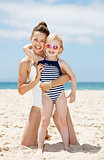 Happy mother and child in swimsuits hugging at sandy beach