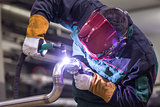 Industrial worker welding in metal factory.