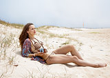 Relaxed bohemian woman with retro photo camera laying on beach