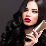 Beautiful brunette model: curls, classic makeup and red lips with a bottle of hair products. The beauty face.