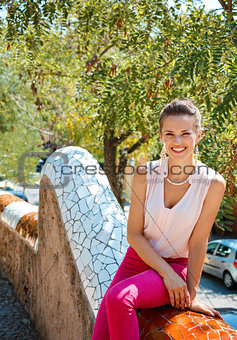 Portrait of happy young woman sitting on trencadis style fence