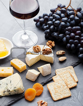 Assortment of cheese with honey, nuts and grape on a modern cutting board slate background.