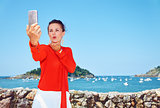 Woman blowing air kiss and taking selfie in front of lagoon