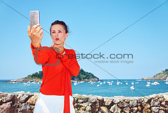 Woman blowing air kiss and taking selfie in front of lagoon