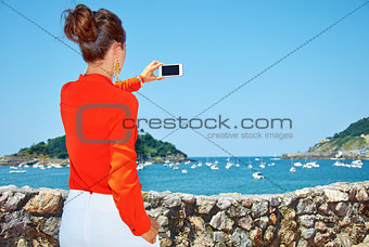 Seen from behind woman taking photo with smartphone of lagoon.