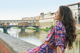 Relaxed woman in dress sitting on embankment near Ponte Vecchio