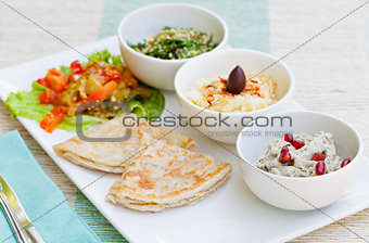 Assortment of dips: hummus, chickpea dip, tabbouleh salad, baba ganoush and flat bread, pita on a plate