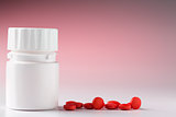 White plastic pill bottle and heap of red pills