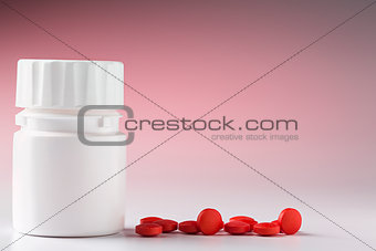 White plastic pill bottle and heap of red pills