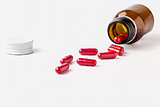 Open glass brown pill bottle and scattered red capsules