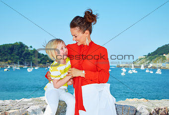 Happy mother playing with child in front of lagoon with yachts