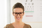 Smiling young woman wearing eyeglasses in front of Snellen chart