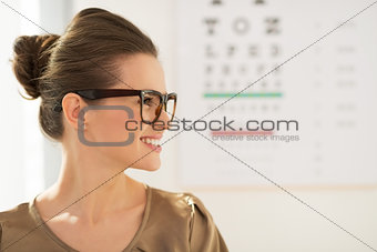Happy young woman wearing eyeglasses in front of Snellen chart