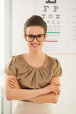 Happy young woman wearing eyeglasses in front of Snellen chart