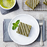 Matcha green tea brownie cake with white chocolate on a white plate Grey stone background