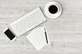 Workplace with cup of coffee, keyboard, smarthphone, white sheets and pen on wooden surface in top view.