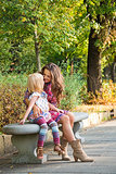 Happy mother and daughter sitting on the bench at the park.