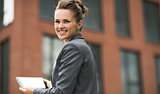 Smiling business woman against office building using tablet PC