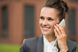 Smiling business woman near office building talking smartphone