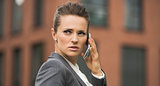 Serious business woman near office building talking smartphone