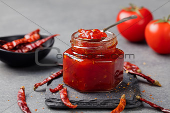 Tomato and chili sauce, jam, confiture in a glass jar on a grey stone background