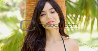 Smiling young woman leaning against a palm