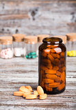 Pills in glass container with other pills on wooden table