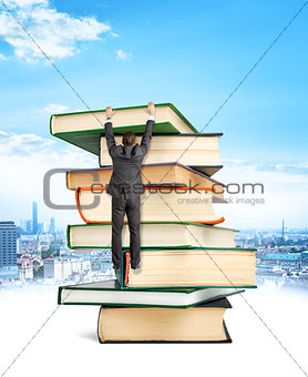 Businessman hanging on top of stack books