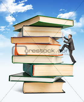 Pile of books with businessman climbing it