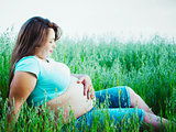 Pregnant woman sitting and looking at her belly outdoors