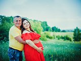 Pregnant woman and her husband with hands on belly outdoors
