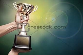 hand holding up a gold trophy cup