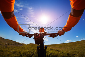 Hands in orange jacket holding handlebar of a bicycle