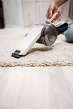 Female hand holding small cordless vacuum cleaner and cleaning rug