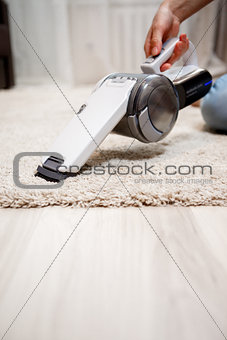 Female hand holding small cordless vacuum cleaner and cleaning rug