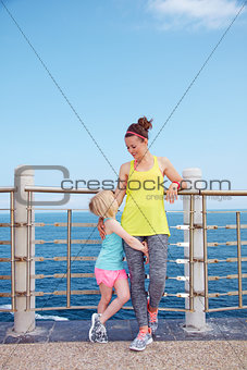 Happy mother and child in fitness outfit standing on embankment