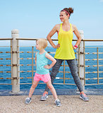 Mother and child in fitness outfit stretching on embankment